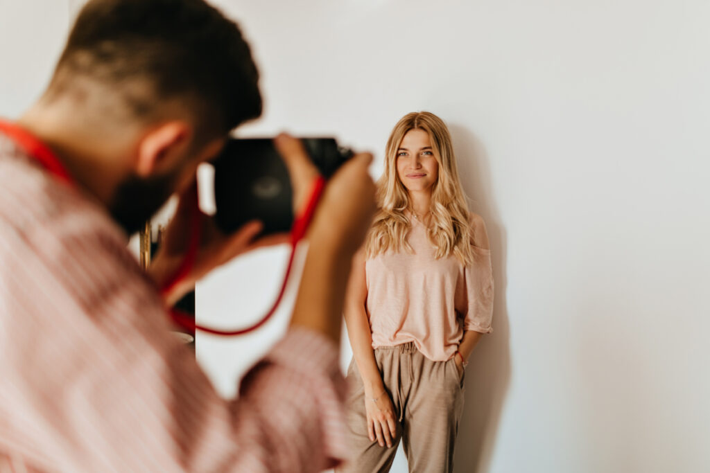dark haired guy makes photo of his blond girlfriend dressed in pink t shirt and beige pants against